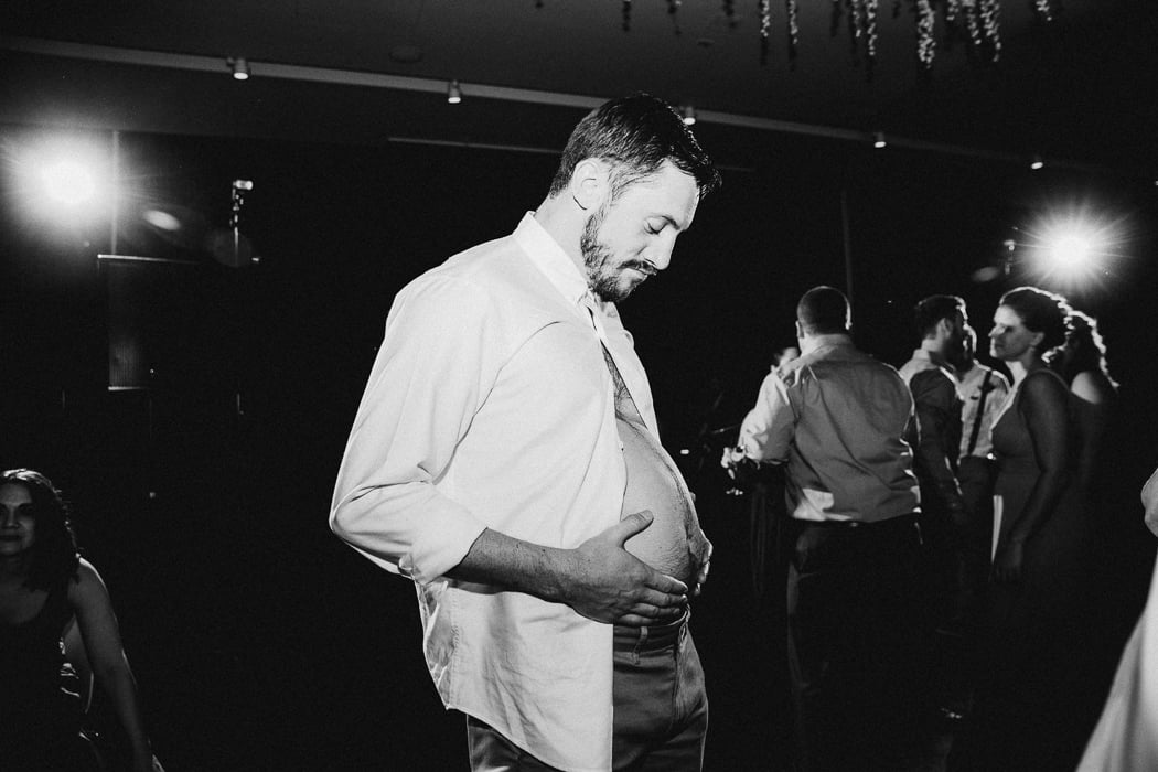 Guy with his shirt unbuttoned rubbing his belly at a wedding.