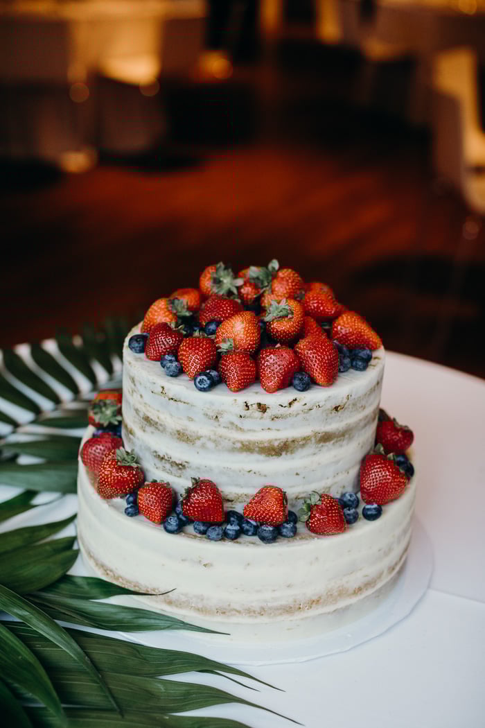Two tier wedding cake with naked frosting and topped with strawberries and blueberries.