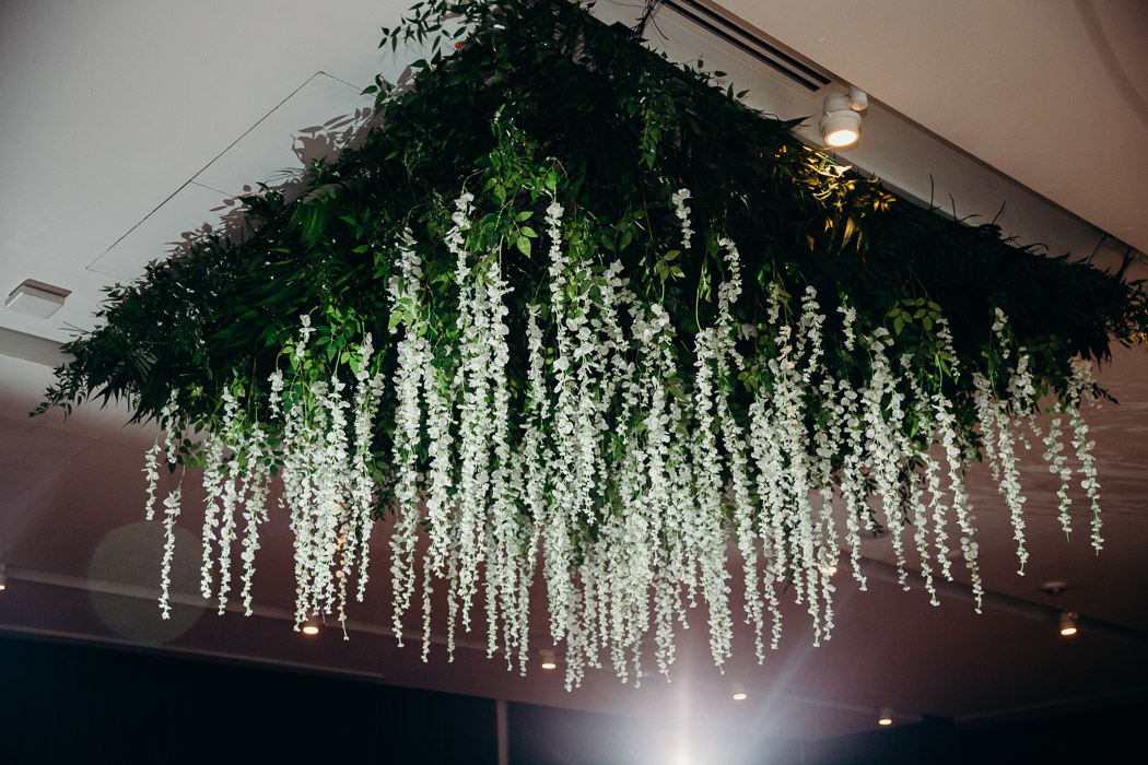 Greenery and flowers hanging from the ceiling at a wedding.