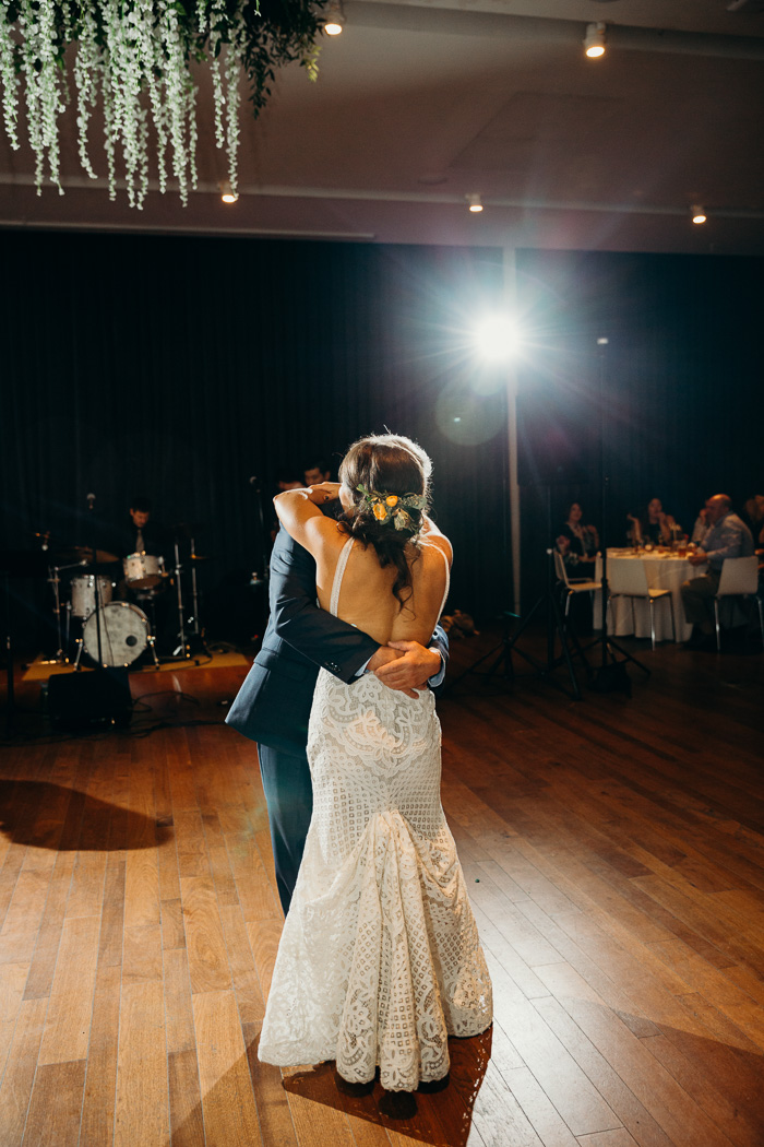 Father and daughter at the daughter's wedding day doing the father and daughter dance. They are embracing and the bride is wearing an open back dress.