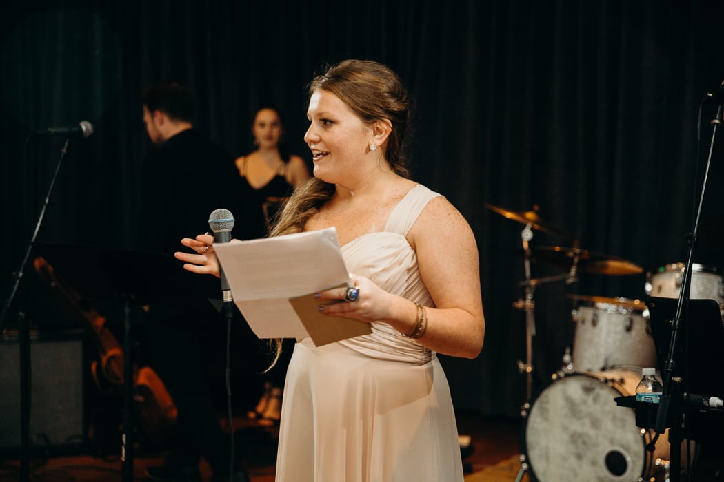 Maid of honor wearing a tan dressing giving a speech at a wedding.