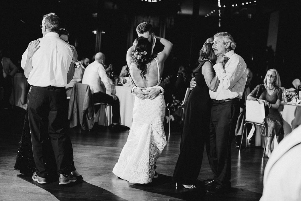 Bride and groom slow dancing with both of their parents slow dancing next to them.