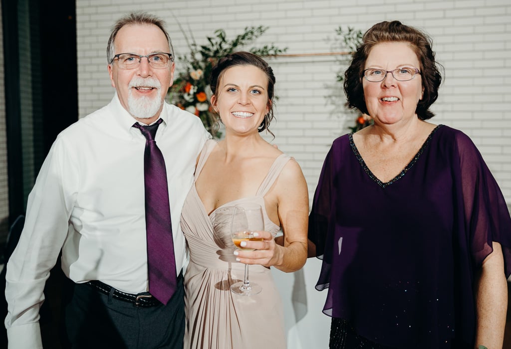 A dad, mom, and their daughter posing for a picture at a wedding.