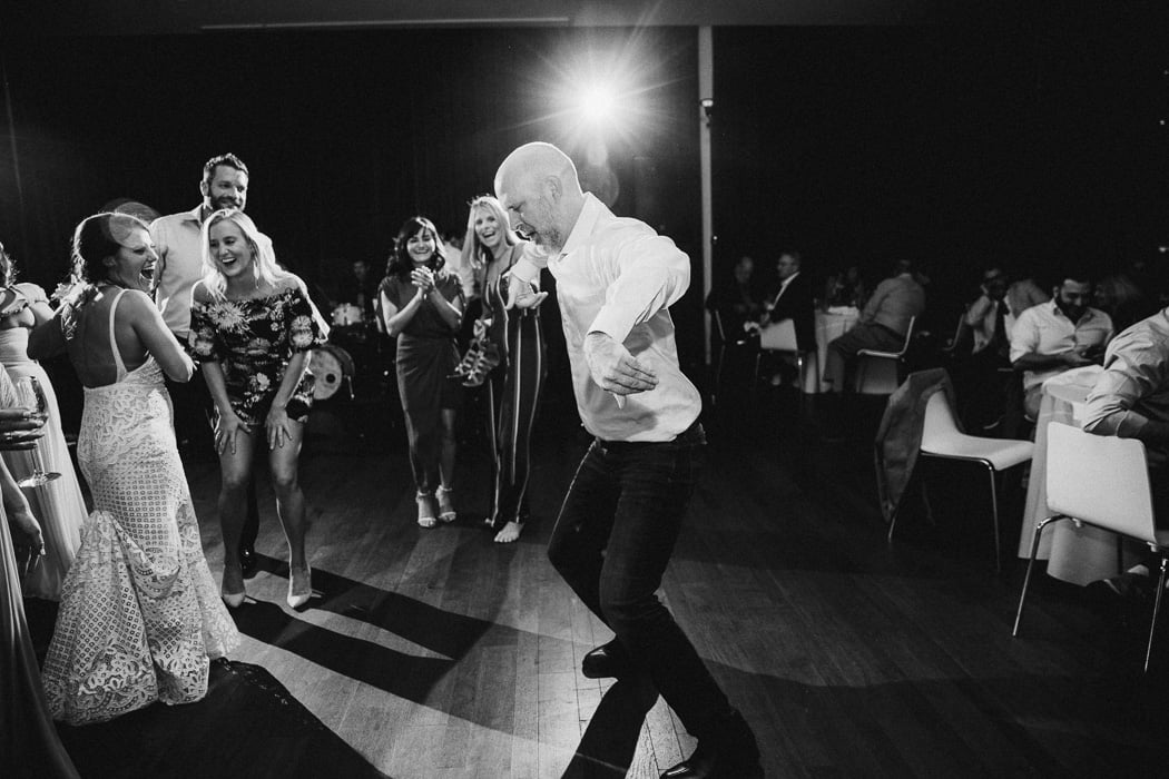 Man dancing in the middle of the dance floor at a wedding with people watching him.