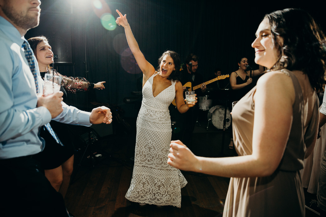 Bride dancing with a cup in one hand and her hand in the air in the other.