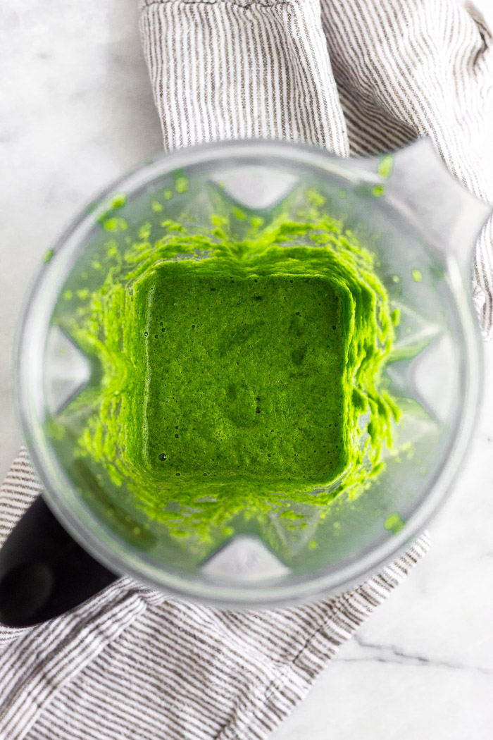 Blender filled with a green puree of herbs, peppers, and broth.