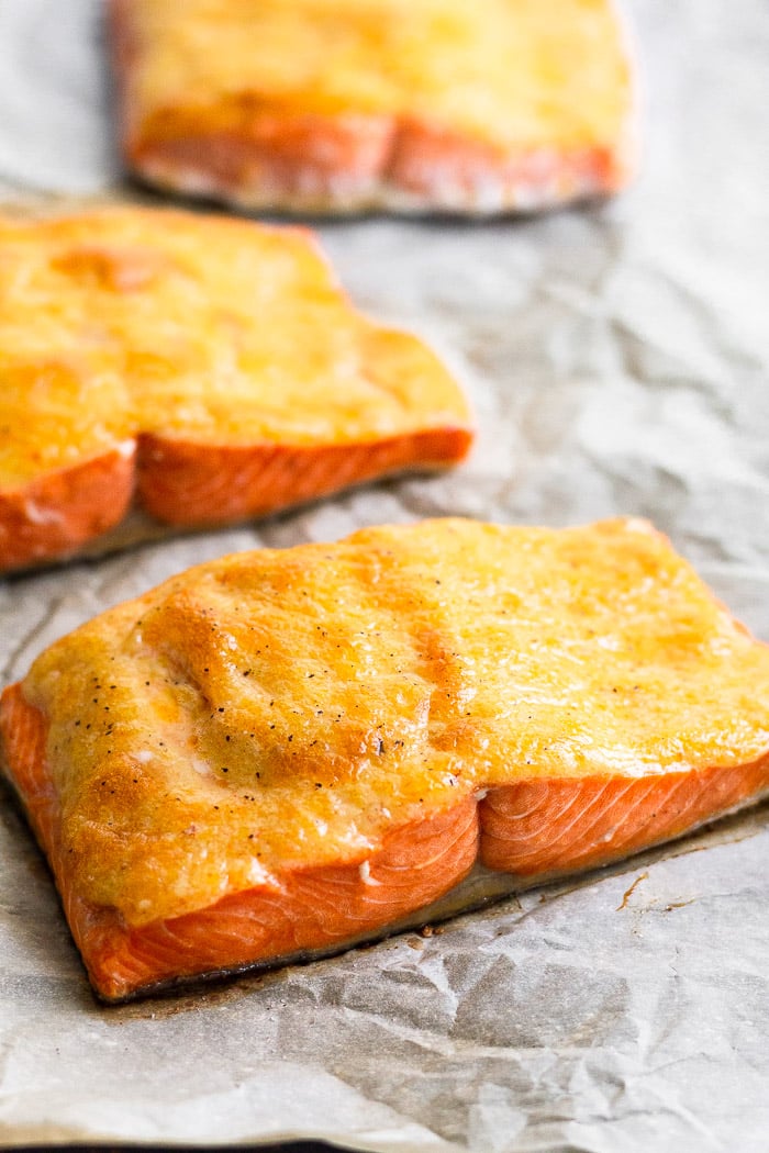 Baking sheet lined with parchment paper with whole30 salmon on it. The salmon is covered in chipotle mayo.