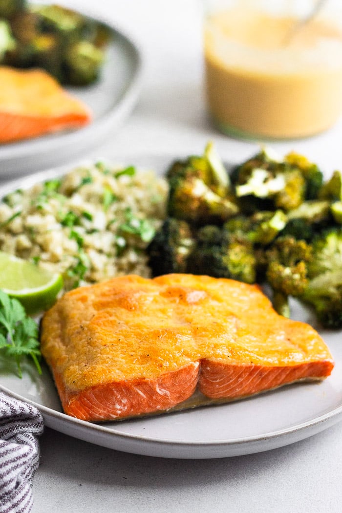 A plate of chipotle salmon made in the air fryer, broccoli, and cauliflower rice. Behind it is jar of chipotle mayo and another plate.