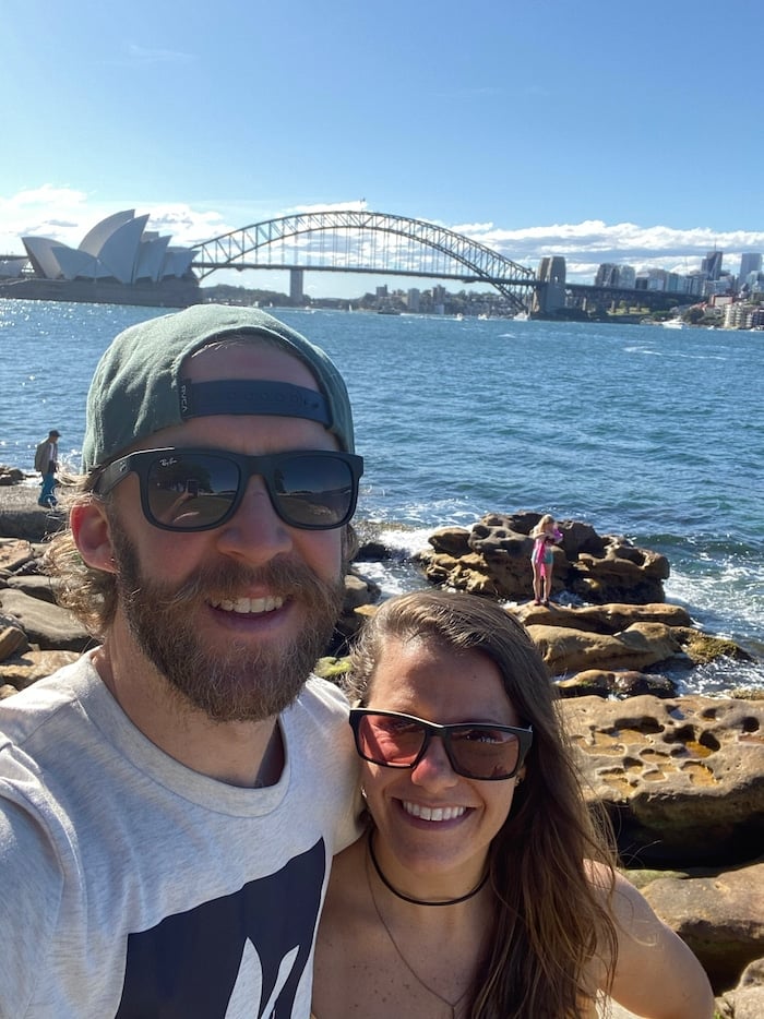 Husband and wife taking a selfie with the Sydney Opera House and bridge behind them.