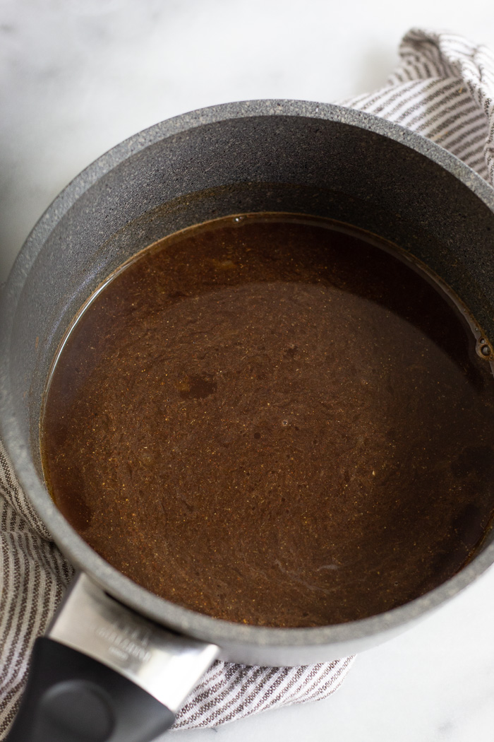 A pan filled with whiskey, coconut aminos, lemon juice, honey, and spices before it is reduced to a glaze.