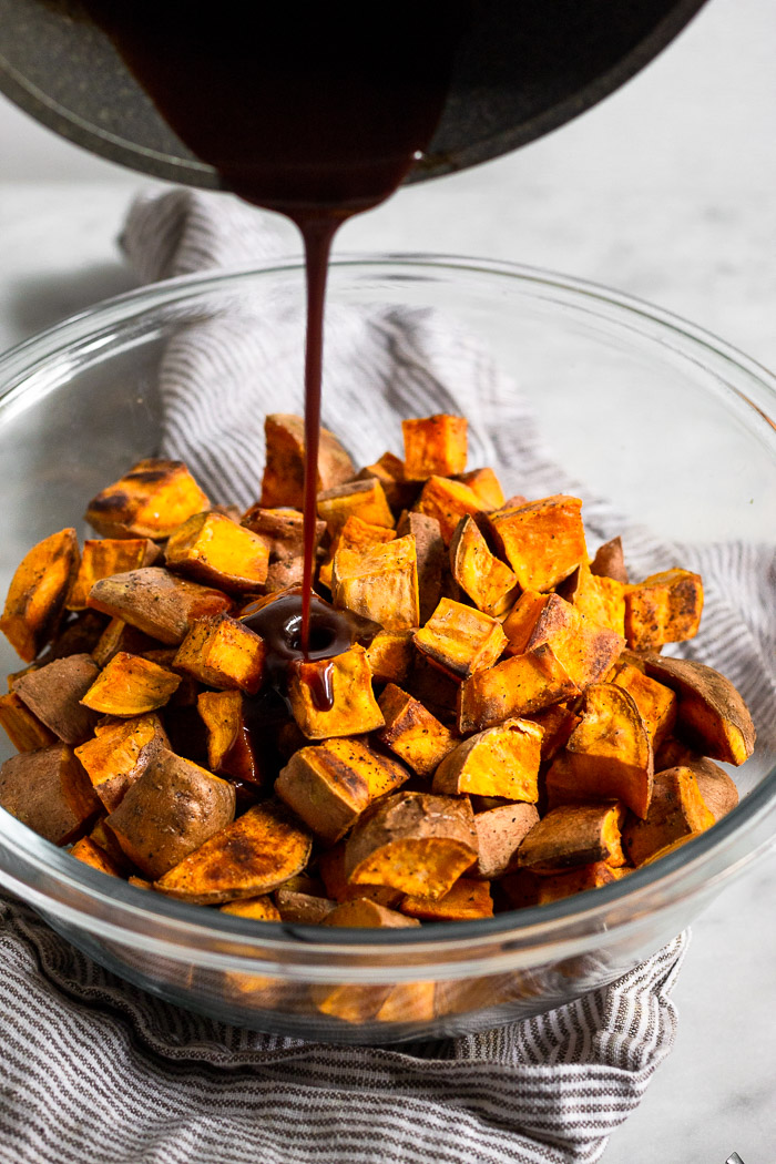 Bowl of roasted sweet potatoes with a whiskey glaze being poured over top of it.