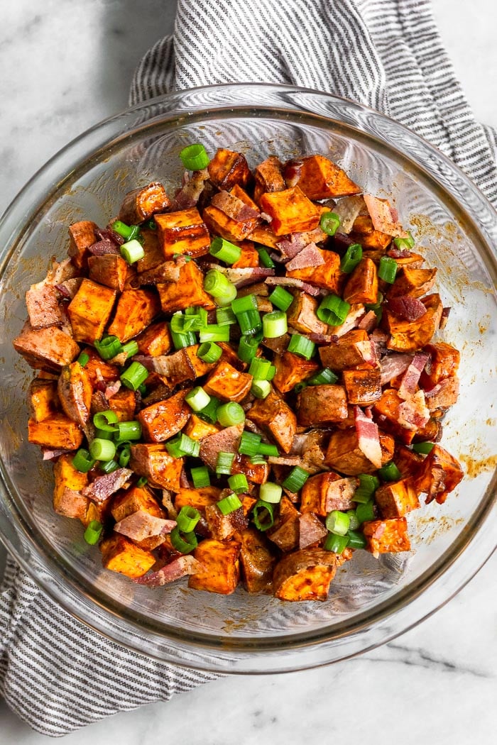 Glass bowl of whiskey sweet potatoes topped with bacon and green onions.