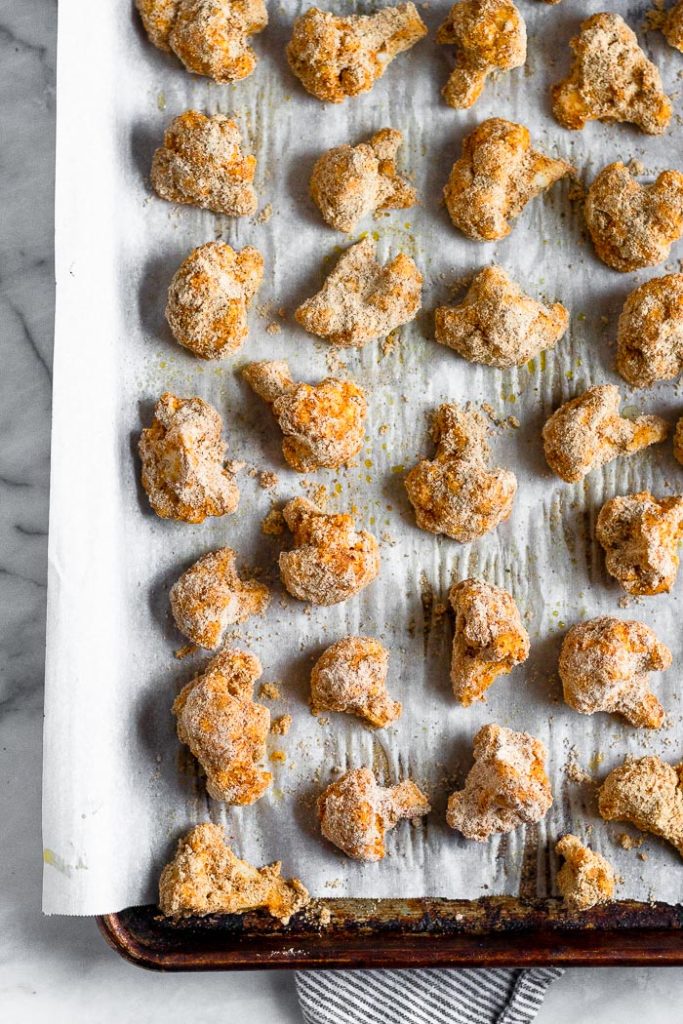 A baking sheet lined with parchment paper with breaded cauliflower florets on it.