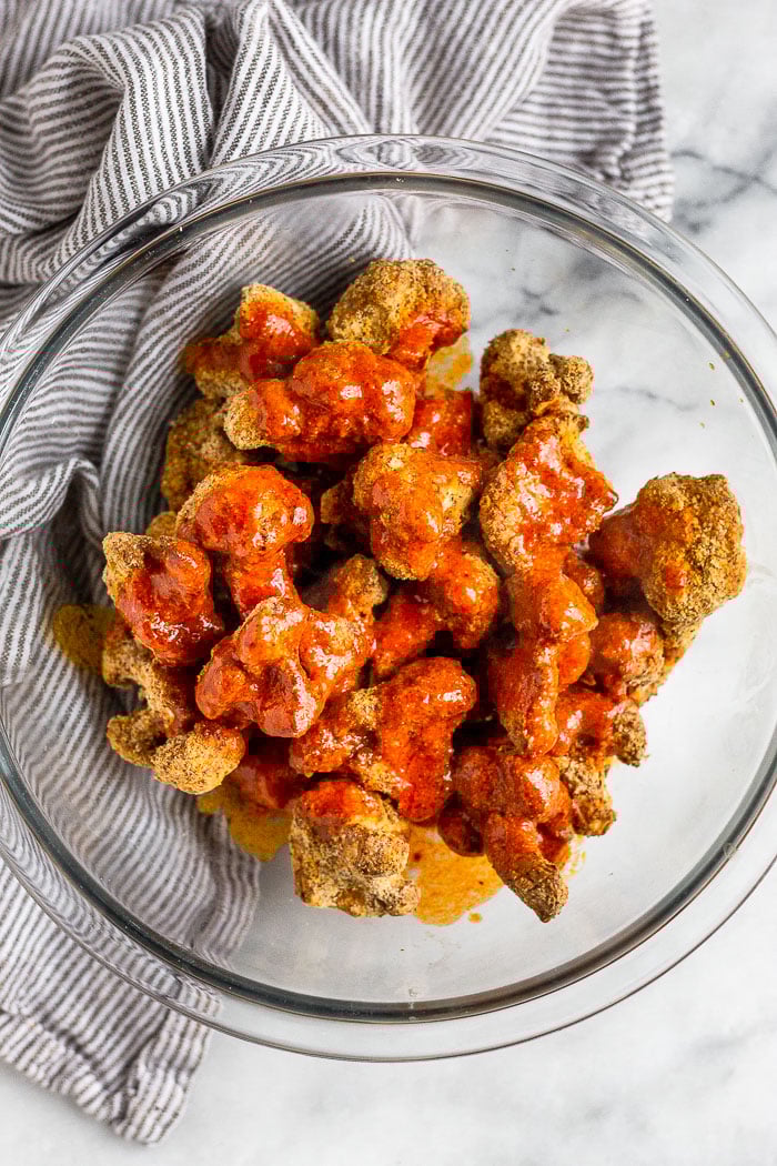 Large glass bowl filled with crispy breaded cauliflower florets and buffalo sauce poured on top of them.