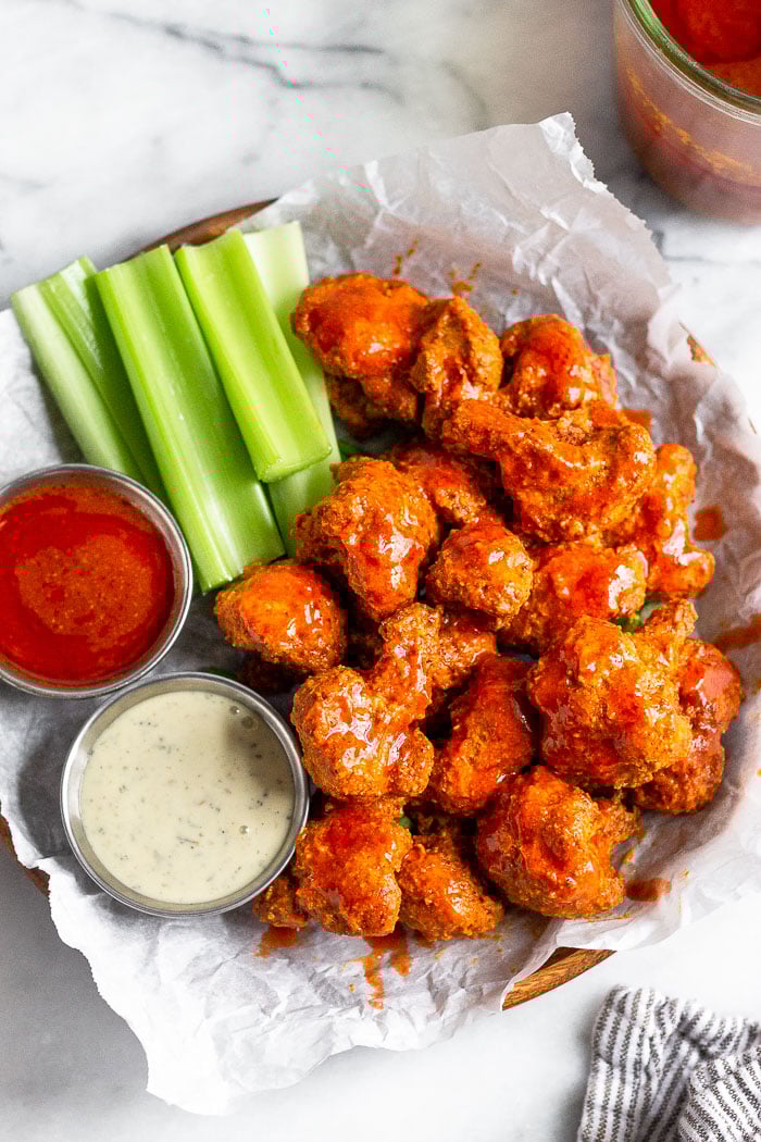 Overhead shot of a plate filled with cauliflower buffalo wings, celery, and to small dishes of ranch and buffalo sauce.