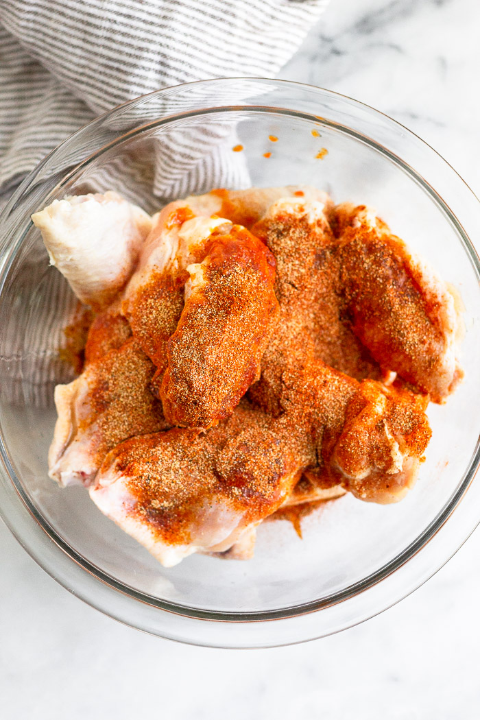 Bowl of raw chicken wings covered in spices.