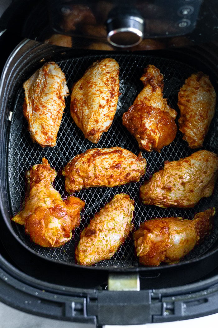 Raw chicken wings coated in spices in an air fryer basket.
