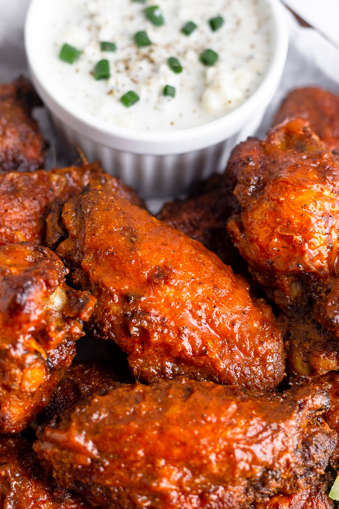 Close up of an air fryer chicken wing surrounded by other wings and a small bowl of blue cheese dressing behind them.