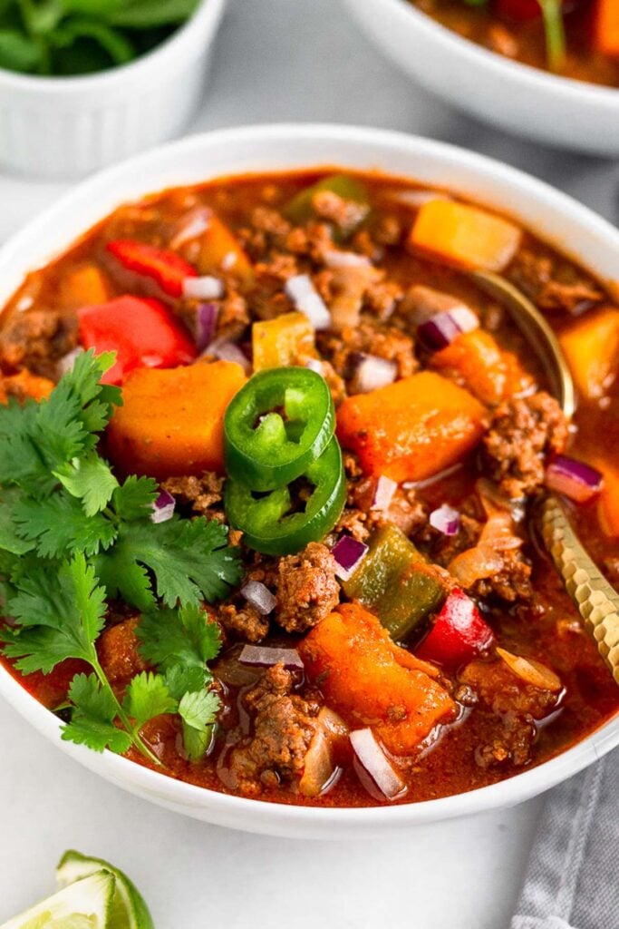 Buffalo chili in a bowl with a spoon in it garnished with cilantro and jalapeños.