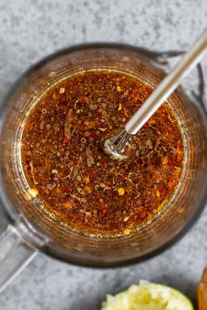 Measuring cup filled with stir fry sauce with a small whisk in it. Next to it is half a juiced lime.