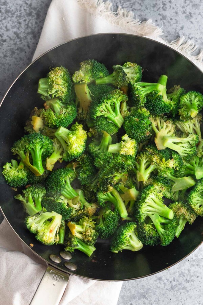 Large skillet filled with sautéed broccoli florets. The pan is sitting on a tan linen.