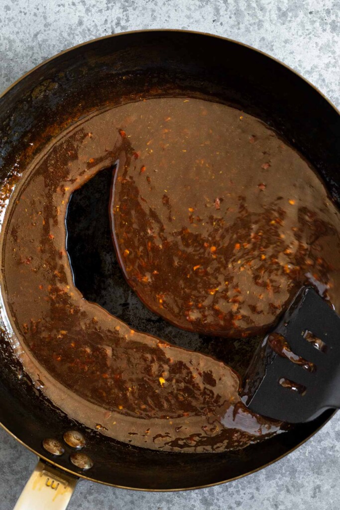 Large skillet filled with a thick brown sauce with a spatula running through it through it and leaving a clean line behind it.