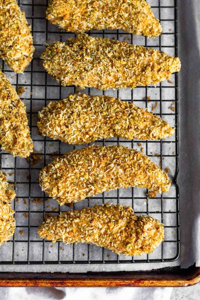 Overhead shot of pistachio chicken tenders on a wire cooling rack on a baking sheet.