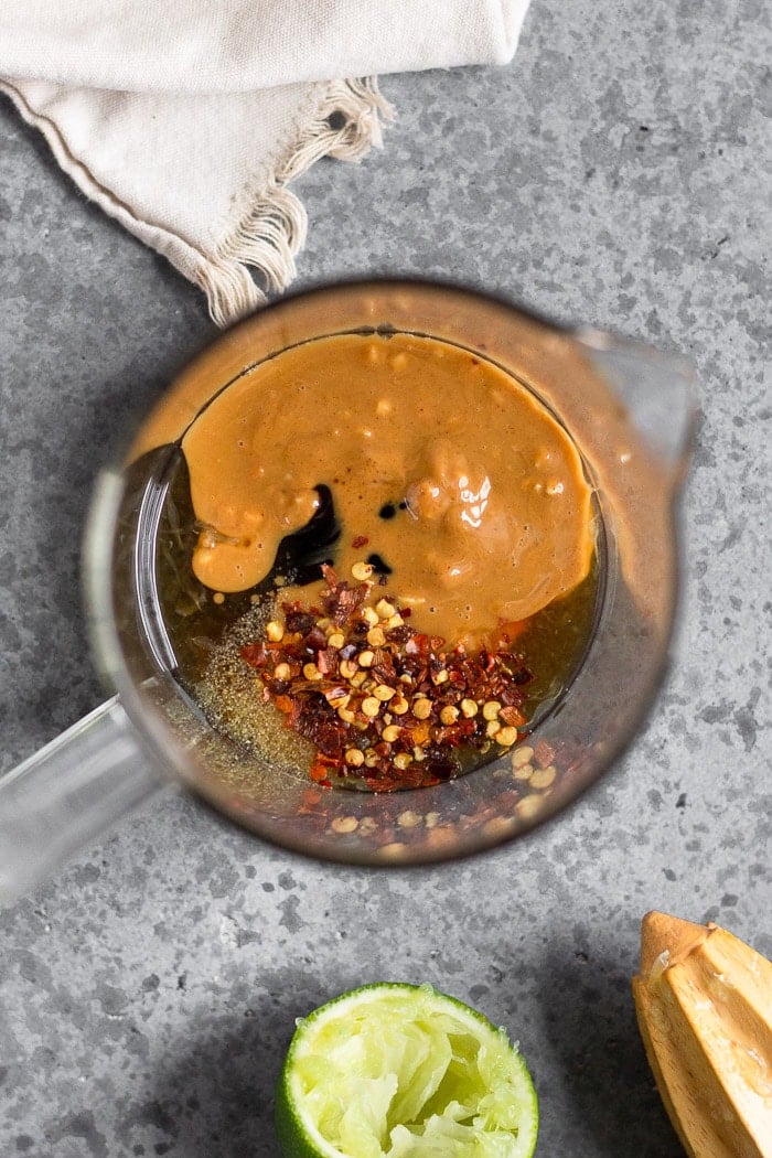 Glass measuring cup filled with coconut aminos, lime juice, vinegar, peanut butter, and spices to make vegan pad thai sauce.