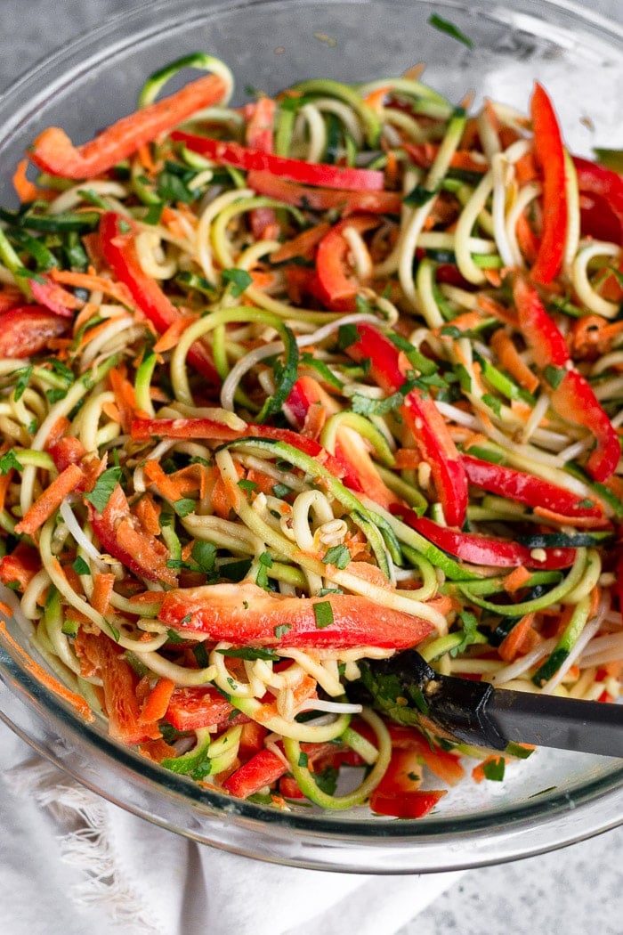 Close up of a large glass bowl of pad thai salad mixed together with a pair of tongs combined out of it.