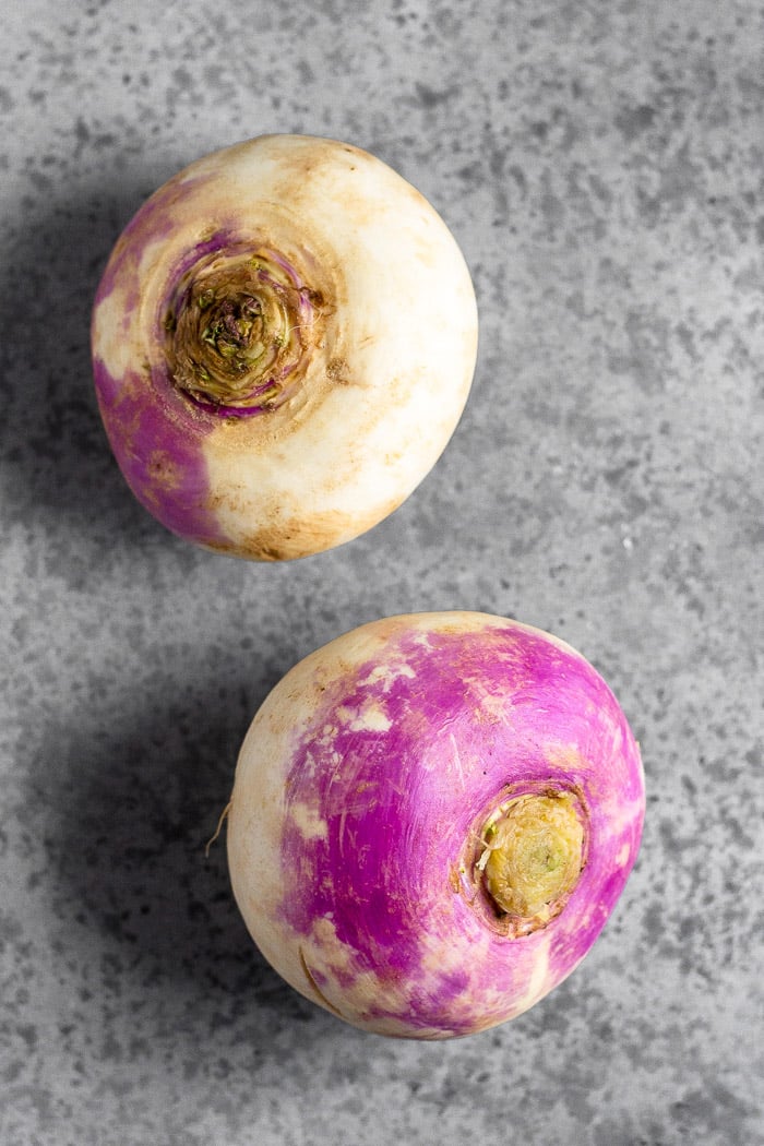 Two large turnips on a grey surface.