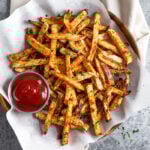 Plate of baked turnip fries and a ramekin of ketchup. The fries are sprinkled with a little parsley.