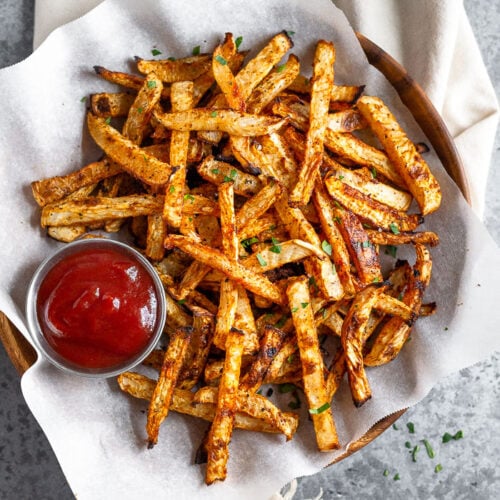 Plate of baked turnip fries and a ramekin of ketchup. The fries are sprinkled with a little parsley.