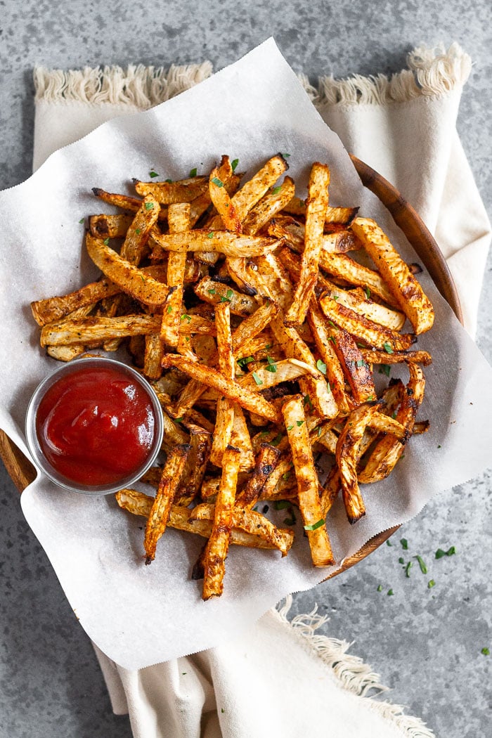 Plate of baked turnip fries and a ramekin of ketchup. The fries are sprinkled with a little parsley.