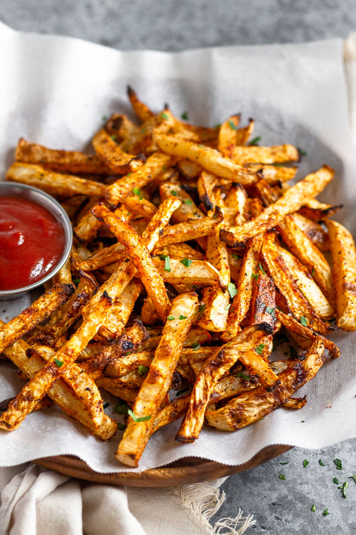 Close up a a plate filled with low carb turnip fries sprinkled with parsley and a small dish of ketchup next to them on the plate.