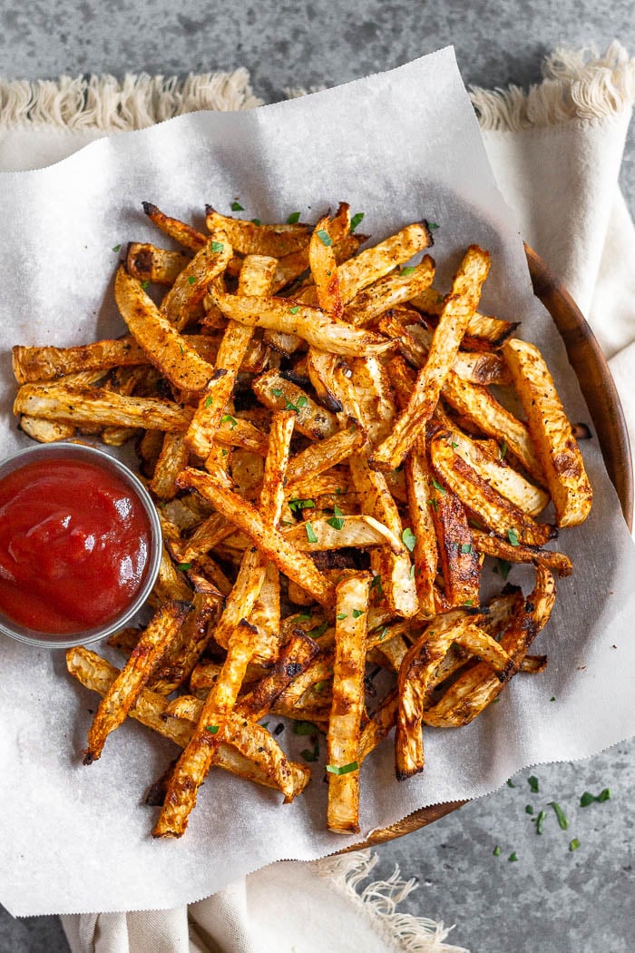 Overhead shot of keto turnip fries sprinkled with parsley and next to a small dish of ketchup. The plate is sitting on a white towel.
