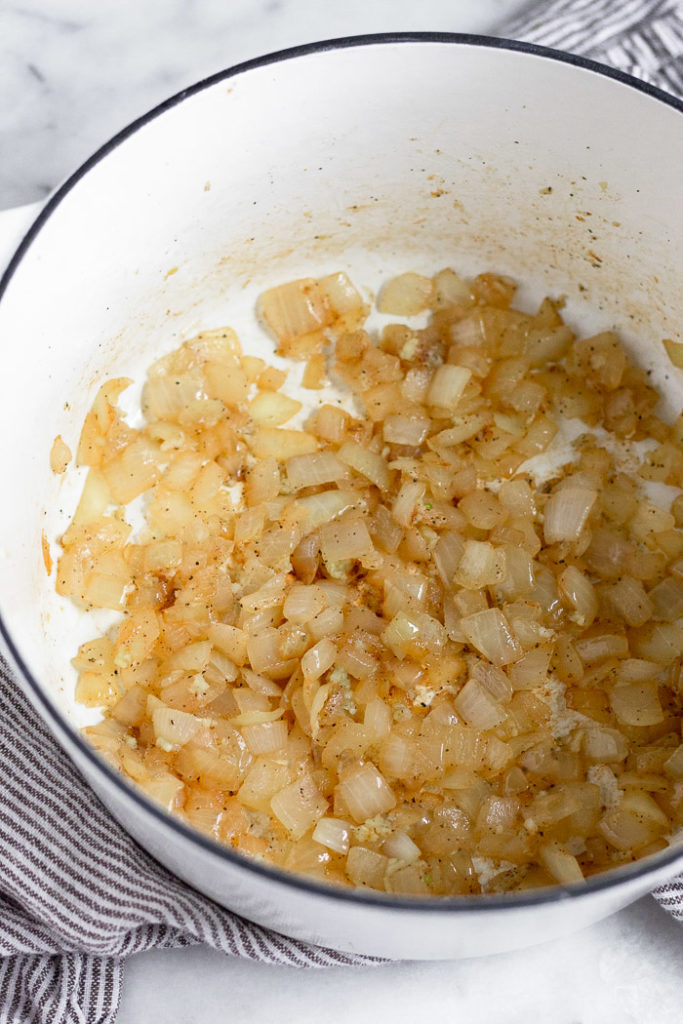 White dutch oven filled with sautéed onions.