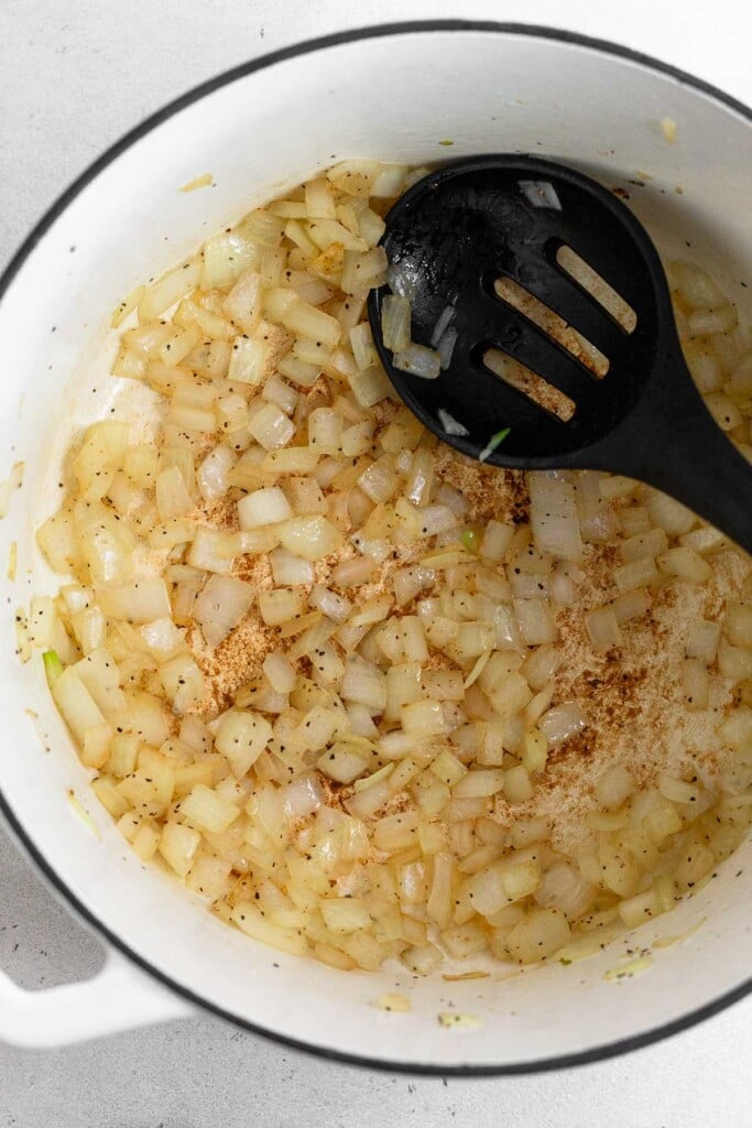 White dutch oven with sautéed onions and a spoon in it.