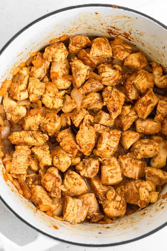 Cubed seasoned chicken breasts and diced onions and in large white dutch oven.
