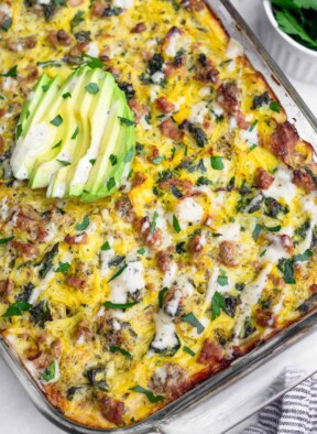 Ground turkey spaghetti squash casserole topped with ranch dressing, parsley, and sliced avocado. Off to the side of the dish is a bowl of more parsley.