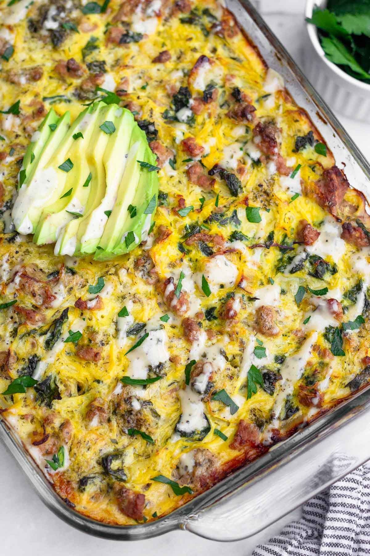 Ground turkey spaghetti squash casserole topped with ranch dressing, parsley, and sliced avocado. Off to the side of the dish is a bowl of more parsley.