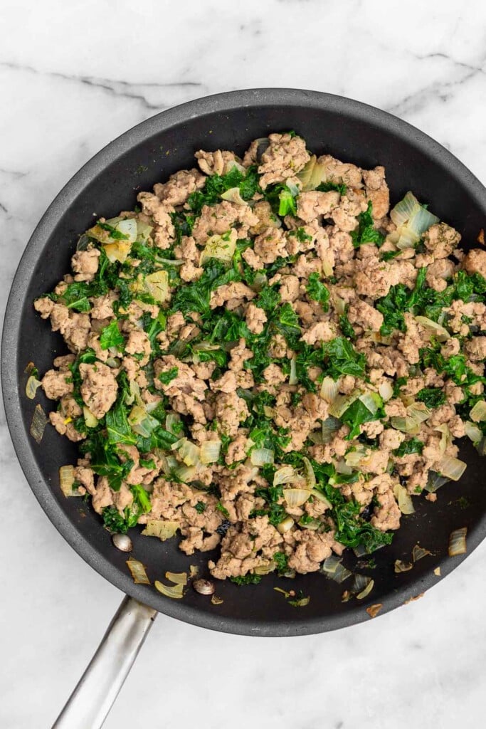 A saute pan filled with cooked ground turkey, kale, onions, and spices.