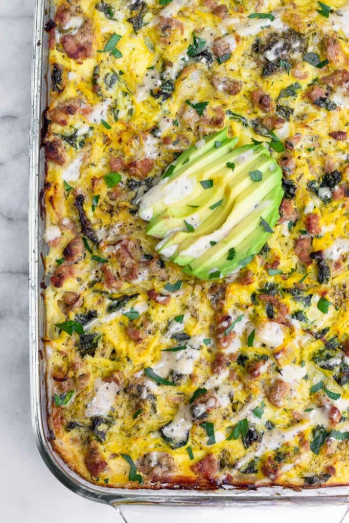 Overhead shot of spaghetti squash ground turkey casserole in a large baking dish. It is topped with sliced avocado, ranch dressing, and parsley.