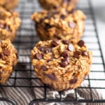 Oatmeal chocolate chip muffins on a cookie drying rack with a striped towel underneath it.