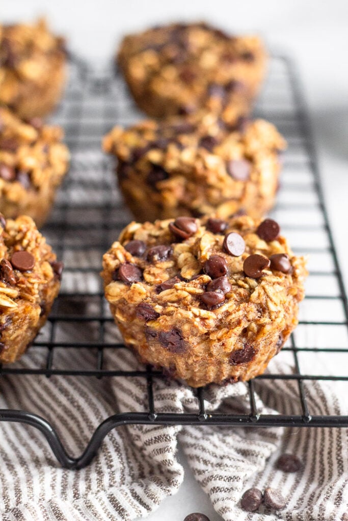 Oatmeal chocolate chip muffins on a cookie drying rack with a striped towel underneath it.