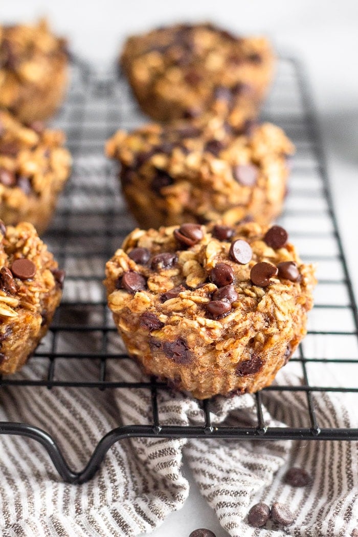Oatmeal chocolate chip muffins on a cookie drying rack with a striped towel underneath it.