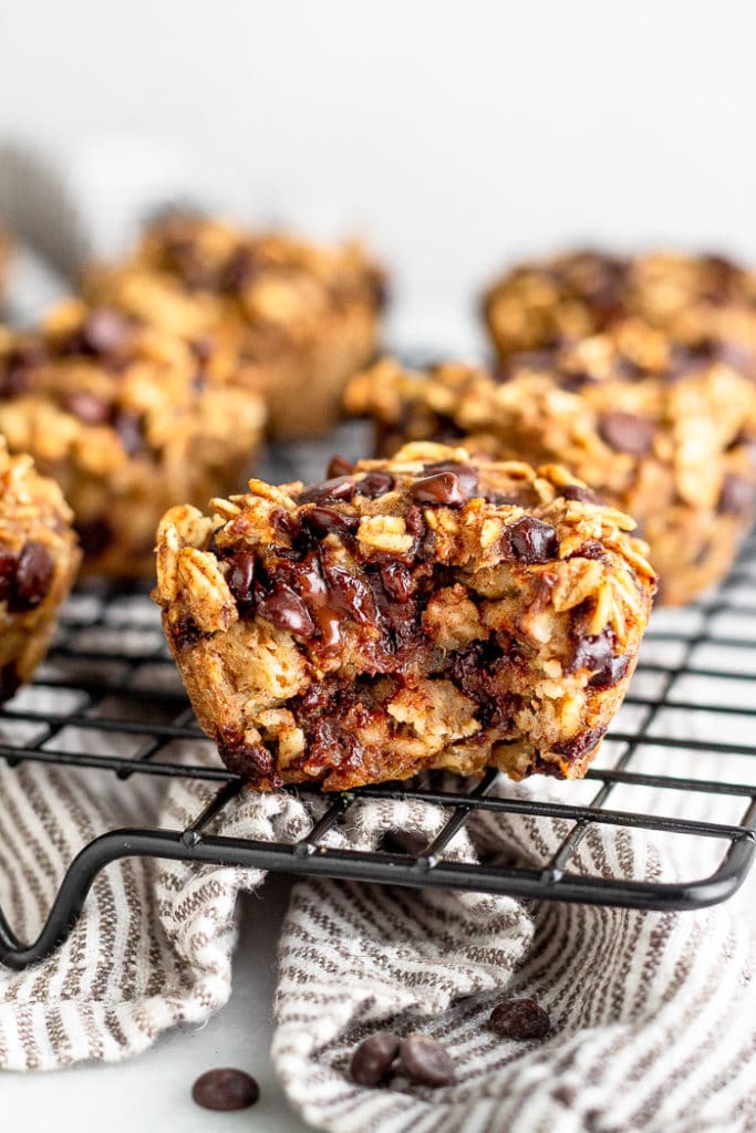 Cookie drying rack filled with banana chocolate chip oatmeal muffins. The one in the from has a bite take out of it and you can see melted chocolate.