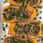 Overhead shot stuffed butternut squash with beef and kale on a baking sheet. There are drizzled with a brown sauce.