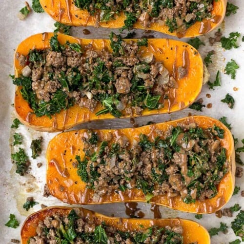 Overhead shot stuffed butternut squash with beef and kale on a baking sheet. There are drizzled with a brown sauce.