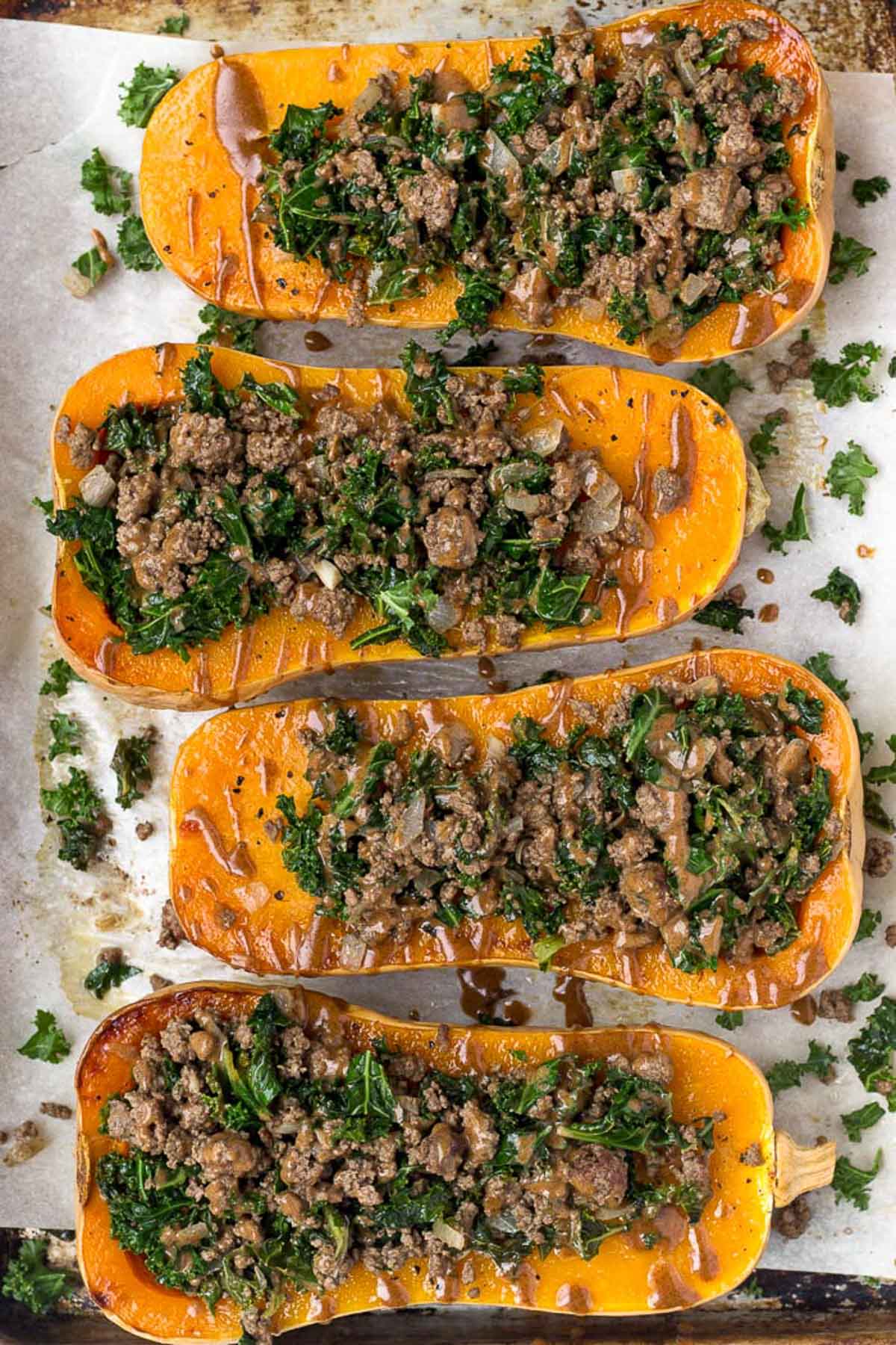 Overhead shot stuffed butternut squash with beef and kale on a baking sheet. There are drizzled with a brown sauce.