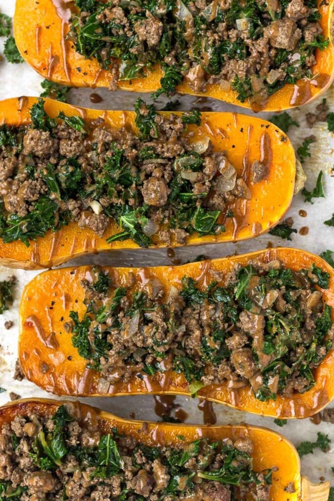 Overhead shot of four halves of butternut squash stuffed with ground beef and kale and drizzled with tahini sauce.
